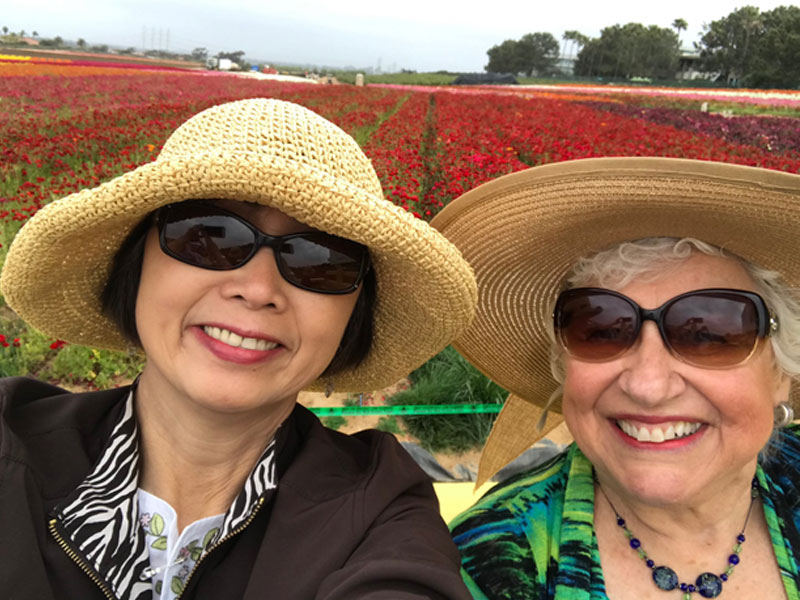Two Ladies Smiling with a Field of Flowers Behind Them